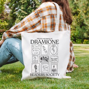 May include: White canvas tote bag with black text and illustrations. The text reads "Proud Member of Dramione Readers Society". The illustrations are of stamps with various Harry Potter themed images.