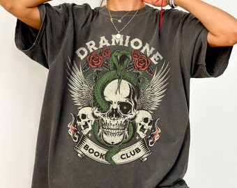May include: A dark gray oversized t-shirt with a graphic print of a skull with wings, a snake, and roses. The text "DRAMIIONE BOOK CLUB" is printed on the shirt.
