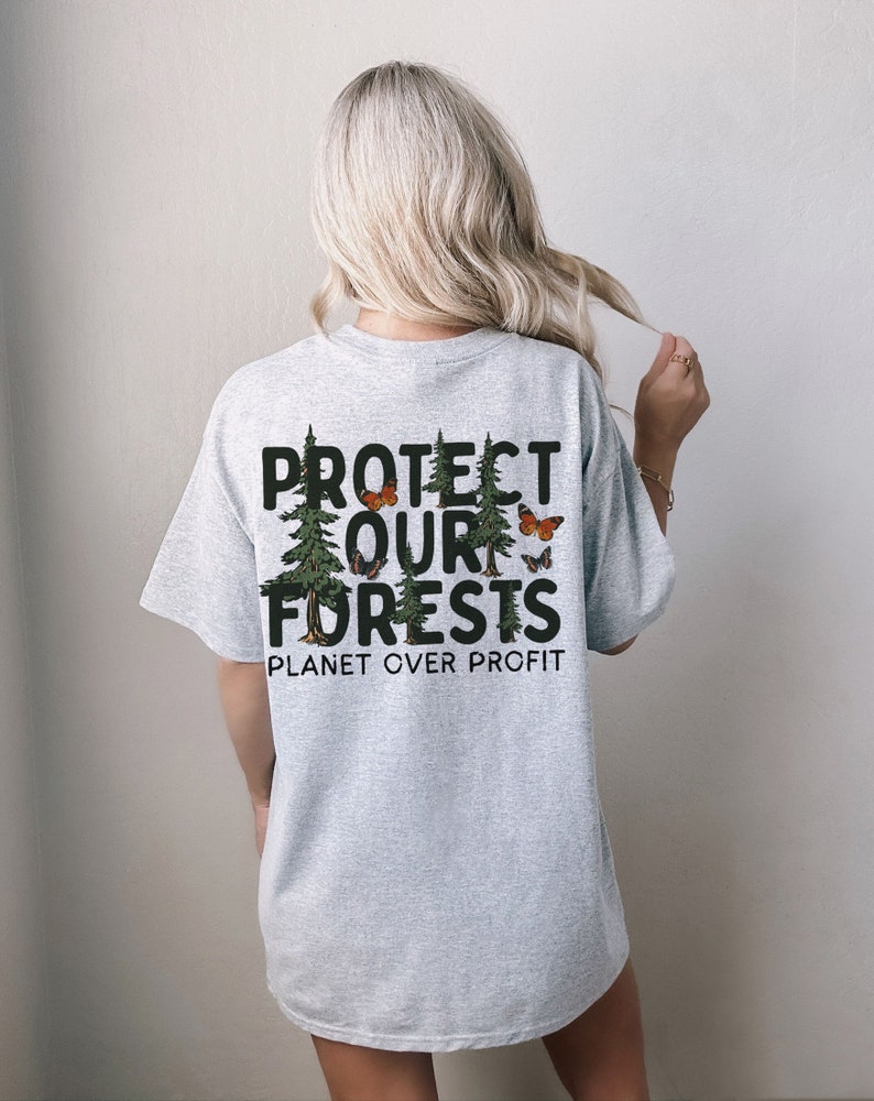 Op de afbeelding: Grijs T-shirt met een grafische print van bomen en vlinders. De tekst op het shirt luidt "Protect Our Forests Planet Over Profit".