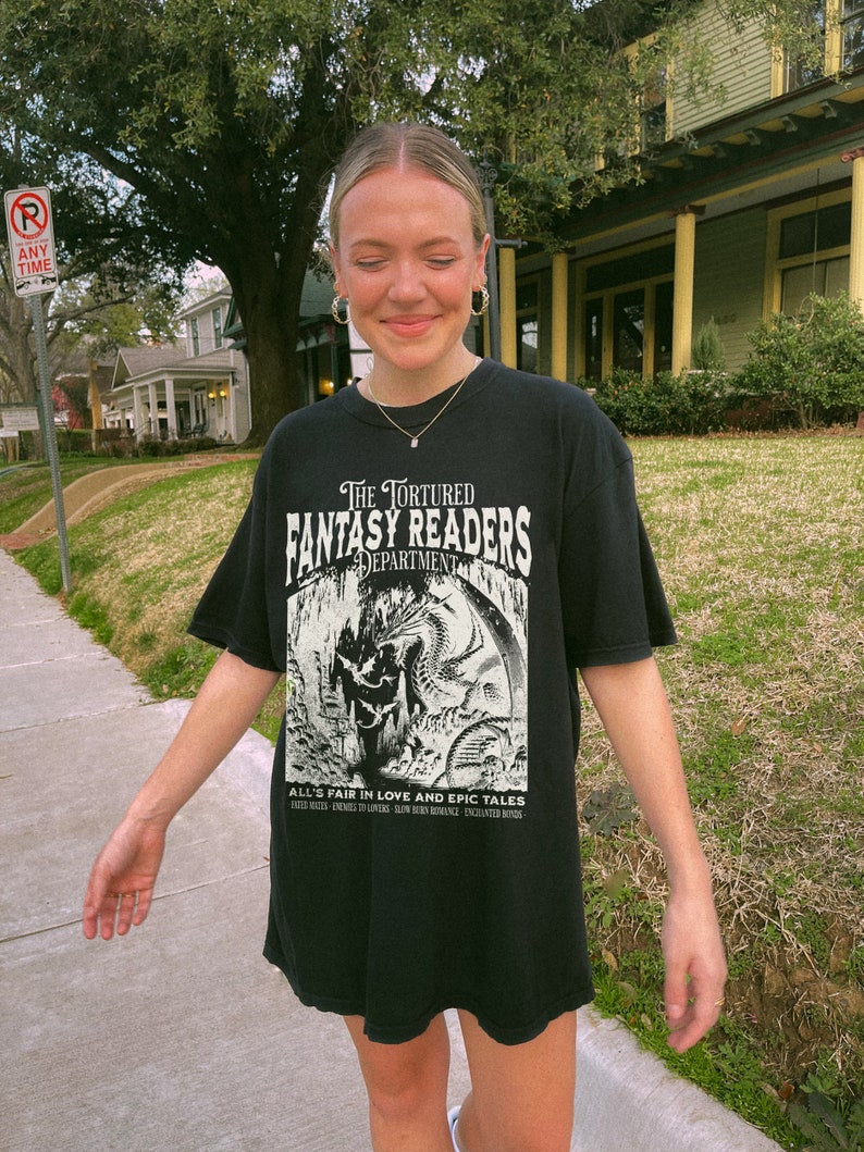 May include: A black t-shirt with a white graphic print of a dragon and the text "The Tortured Fantasy Readers Department" and "All's Fair in Love and Epic Tales".