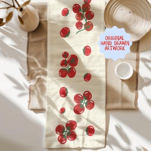 May include: Cream-colored table runner with a repeating pattern of red tomatoes and green stems. The words "ORIGINAL HAND DRAWN ARTWORK" are in a blue bubble. The runner is on a beige surface.