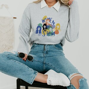 May include: A gray sweatshirt with a graphic print of women in STEM. The graphic features a group of women with colorful outlines and the text "Women in STEM".
