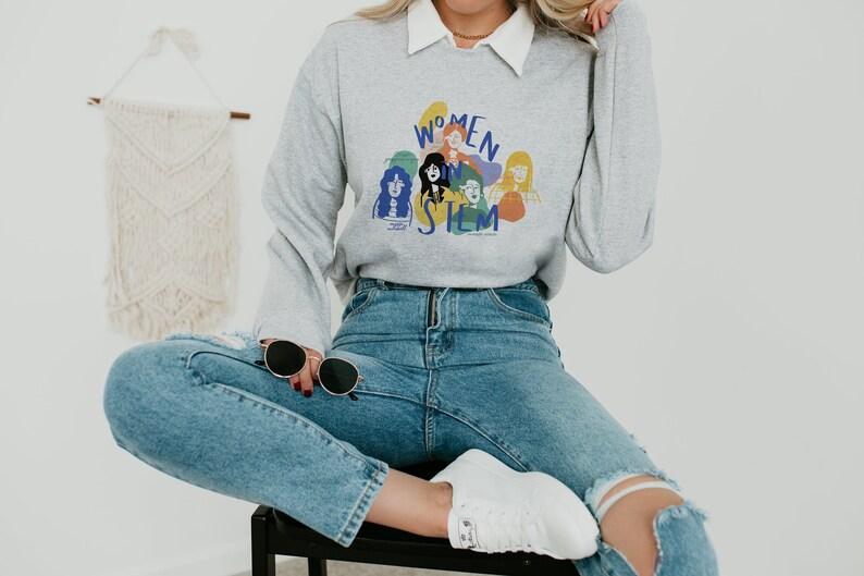 May include: A gray sweatshirt with a graphic print of women in STEM. The graphic features a group of women with colorful outlines and the text "Women in STEM".