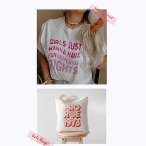 May include: Two tote bags with feminist slogans printed on them. The first tote bag features a white t-shirt with the text "Girls Just Wanna Have Fundamental Rights" printed in pink. The second tote bag features a white canvas tote bag with the text "Pro Roe 1973" printed in orange.