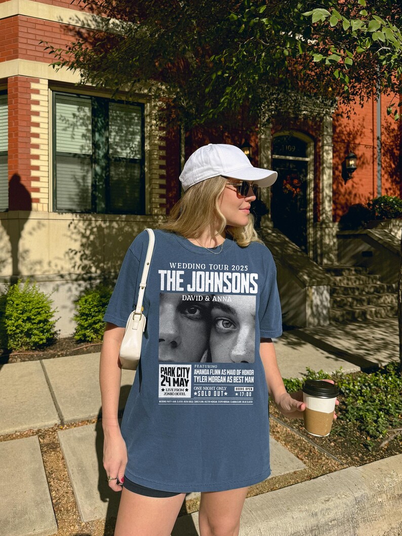May include: A blue t-shirt with a white print of a wedding tour poster for "The Johnsons, David & Anna". The poster features a black and white photo of a couple's eyes and includes the date "24 May" and the location "Park City".
