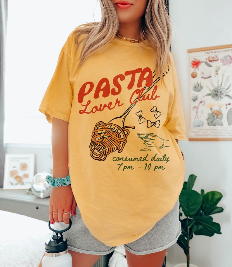 May include: Yellow short-sleeved t-shirt with a graphic print of a fork with spaghetti and the text "Pasta Lover Club consumed daily 7pm - 10pm".