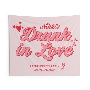 May include: Pink bachelorette party tapestry with the text "Nikki's Drunk in Love" in red and pink lettering. The text "Bachelorette Party Las Vegas 2024" is also included in smaller red lettering.