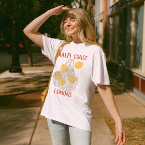 May include: A white t-shirt with a graphic of lemons in a mesh bag and the text "Malfi Coast Lemons".