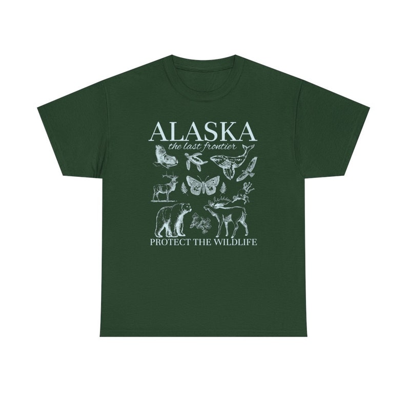 Puede incluir: Una camiseta verde oscuro con un dise&ntilde;o gr&aacute;fico blanco que presenta el texto "Alaska the last frontier" e ilustraciones de diversas especies de vida silvestre de Alaska, incluyendo un oso, una ballena, un alce, una mariposa y un p&aacute;jaro. El texto "Protect the Wildlife" est&aacute; impreso debajo de las ilustraciones.