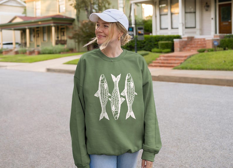 May include: A green sweatshirt with a white graphic of three fish. The fish are stylized and have a geometric pattern.