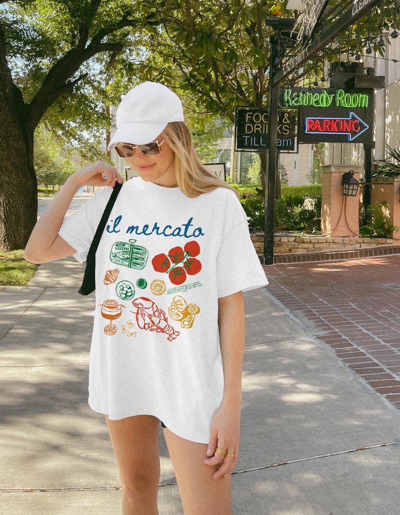 Op de afbeelding: Wit T-shirt met een grafische print van verschillende Italiaanse voedingsmiddelen en de tekst "il mercato".