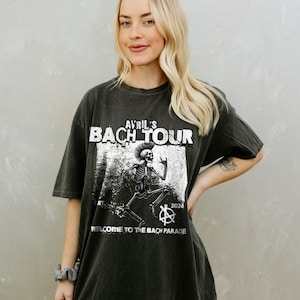 Puede incluir: Una camiseta negra de gran tamaño con un estampado gráfico blanco de un esqueleto con un mohawk tocando la guitarra. El texto "Avril's Bach Tour" está impreso sobre el esqueleto y "Welcome to the Bach Parade" está impreso debajo del esqueleto. El texto "Est. 2024" está impreso a la derecha del esqueleto.