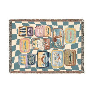 May include: A woven throw blanket featuring a repeating pattern of sardine tins in various colors and designs. The blanket has a checkered blue and cream background and fringed edges. The sardine tins have text on them.