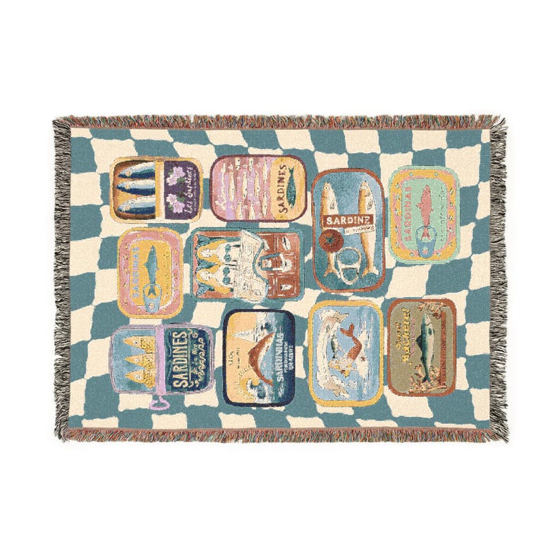 May include: A woven throw blanket featuring a repeating pattern of sardine tins in various colors and designs. The blanket has a checkered blue and cream background and fringed edges. The sardine tins have text on them.
