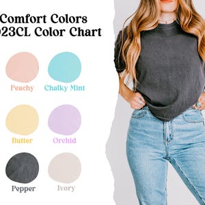 May include: A woman wearing a dark gray t-shirt and light blue jeans. The image includes a color chart with the text "Comfort Colors 3023CL Color Chart" and color swatches labeled Peachy, Chalky Mint, Butter, Orchid, Pepper, and Ivory.