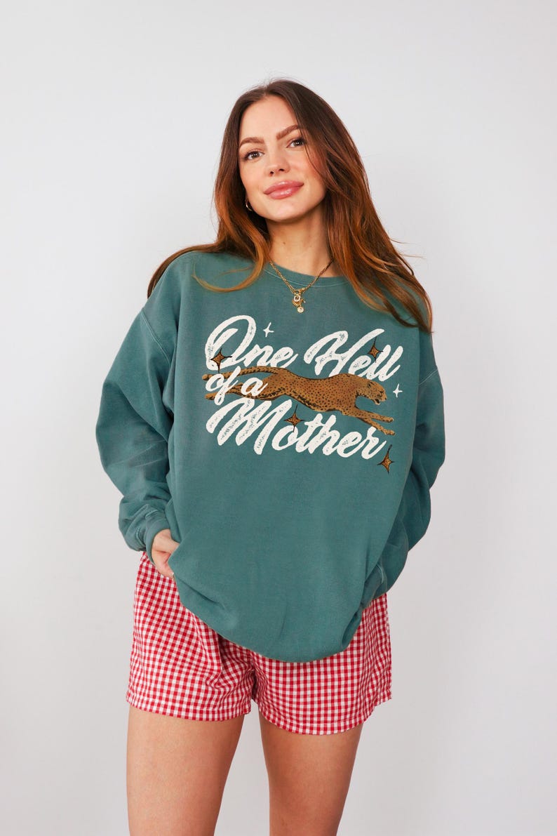 Peut inclure: Sweat-shirt bleu sarcelle avec un imprim&eacute; graphique blanc d'un gu&eacute;pard courant et le texte "One Hell of a Mother".