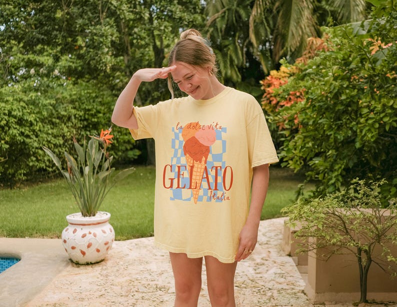 K&ouml;nnte beinhalten: Eine Frau tr&auml;gt ein gelbes T-Shirt mit einem Aufdruck eines Eisbechers und dem Text "La dolce vita Gelato Italia".
