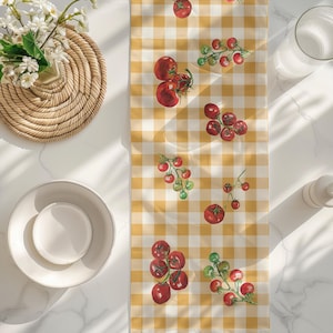 May include: A yellow and white checkered table runner with a red tomato design. The runner features clusters of tomatoes and individual tomatoes on a vine.