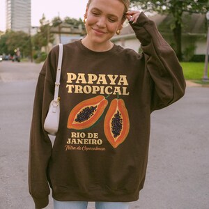 Puede incluir: Sudadera marr&oacute;n con un gr&aacute;fico de papaya y el texto "Papaya Tropical Rio de Janeiro Feira de Copacabana".