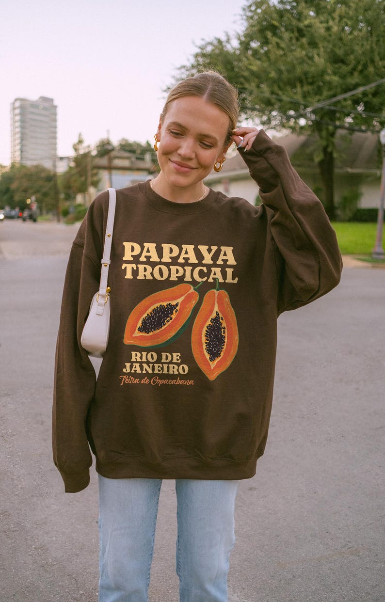 Puede incluir: Sudadera marr&oacute;n con un gr&aacute;fico de papaya y el texto "Papaya Tropical Rio de Janeiro Feira de Copacabana".