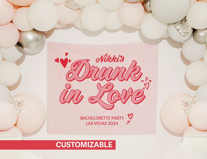 May include: Pink and white bachelorette party banner with the text "Nikki's Drunk in Love" in red and white lettering. The banner also includes the text "Bachelorette Party Las Vegas 2024" in smaller red lettering.