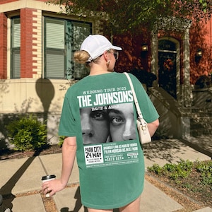 May include: A green t-shirt with a white print of a wedding announcement for "The Johnsons" with the text "Wedding Tour 2025" and "David & Anna". The announcement features a black and white photo of a couple's eyes. The text also includes "Park City 24 May" and "Sold Out".