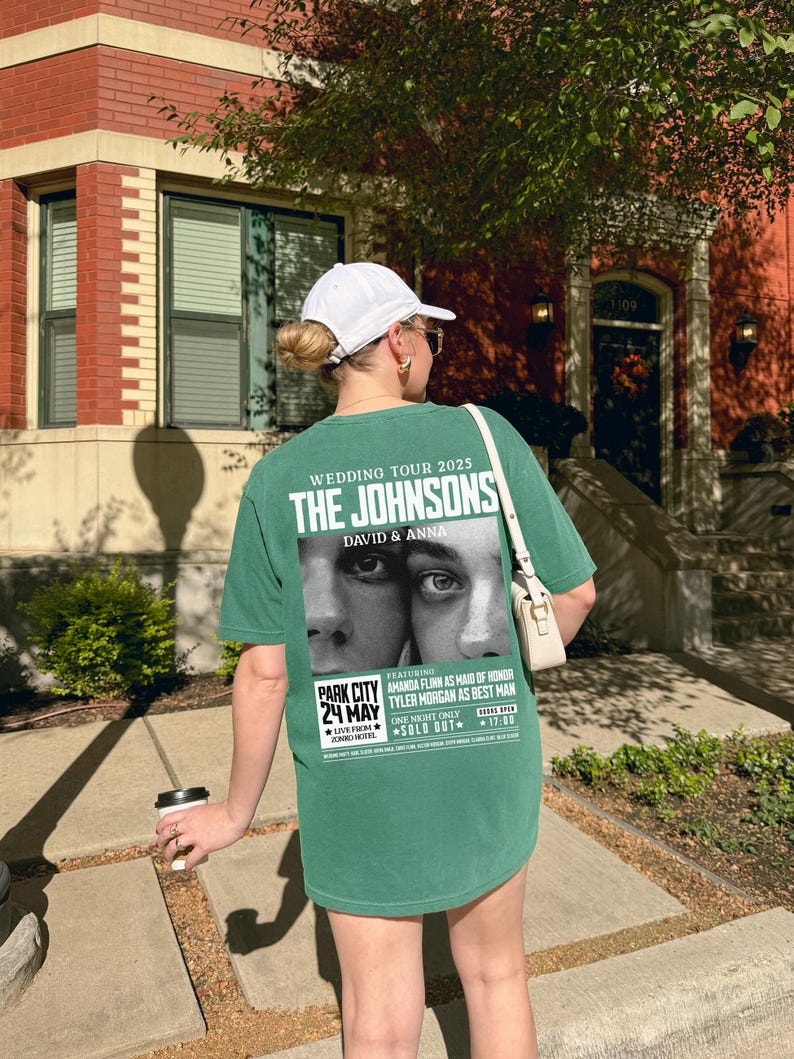 May include: A green t-shirt with a white print of a wedding announcement for "The Johnsons" with the text "Wedding Tour 2025" and "David & Anna". The announcement features a black and white photo of a couple's eyes. The text also includes "Park City 24 May" and "Sold Out".