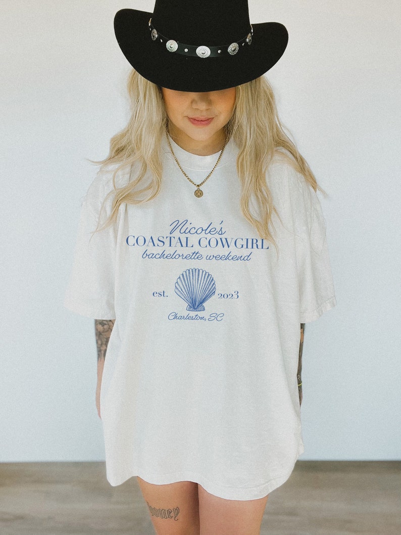 K&ouml;nnte beinhalten: Wei&szlig;es T-Shirt mit einem blauen Grafikdesign, auf dem "Nicole's Coastal Cowgirl bachelorette weekend est. 2023 Charleston, SC" steht, mit einer blauen Muschelillustration.