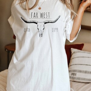 K&ouml;nnte beinhalten: Wei&szlig;es Oversize-T-Shirt mit einer schwarzen Grafik eines Sch&auml;dels mit H&ouml;rnern und dem Text "FAR WEST ESTD 1899".