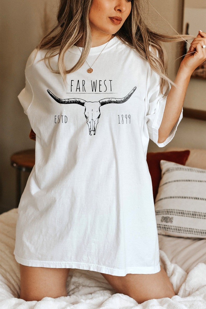 K&ouml;nnte beinhalten: Wei&szlig;es Oversize-T-Shirt mit einer schwarzen Grafik eines Sch&auml;dels mit H&ouml;rnern und dem Text "FAR WEST ESTD 1899".