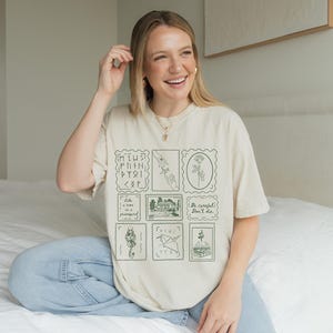 May include: Cream-colored t-shirt featuring a collection of green postage stamp designs. The stamps depict various illustrations, including a hand, a flower, and a snake. The shirt also includes the text "Be careful, don't die."