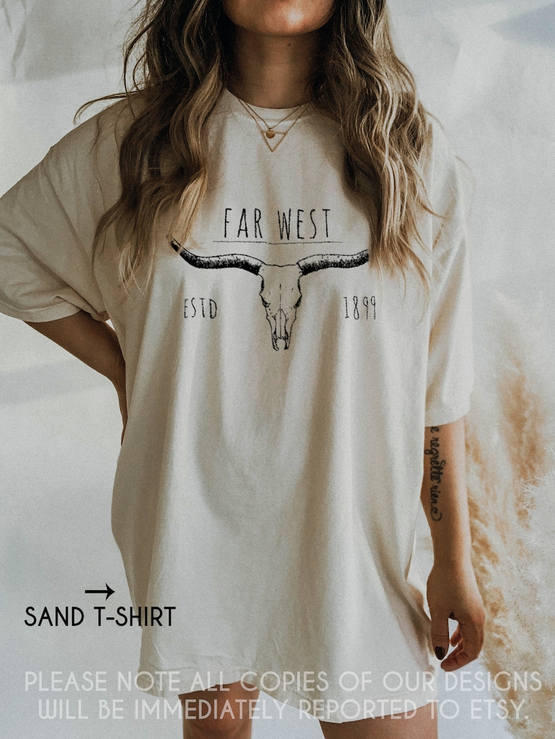 K&ouml;nnte beinhalten: Ein sandfarbenes T-Shirt mit einem schwarzen Aufdruck eines Sch&auml;dels mit H&ouml;rnern und dem Text "FAR WEST ESTD 1899".