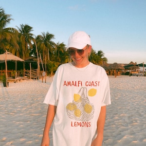 May include: White oversized t-shirt with a graphic of lemons in a mesh bag and the text "Amalfi Coast Lemons".