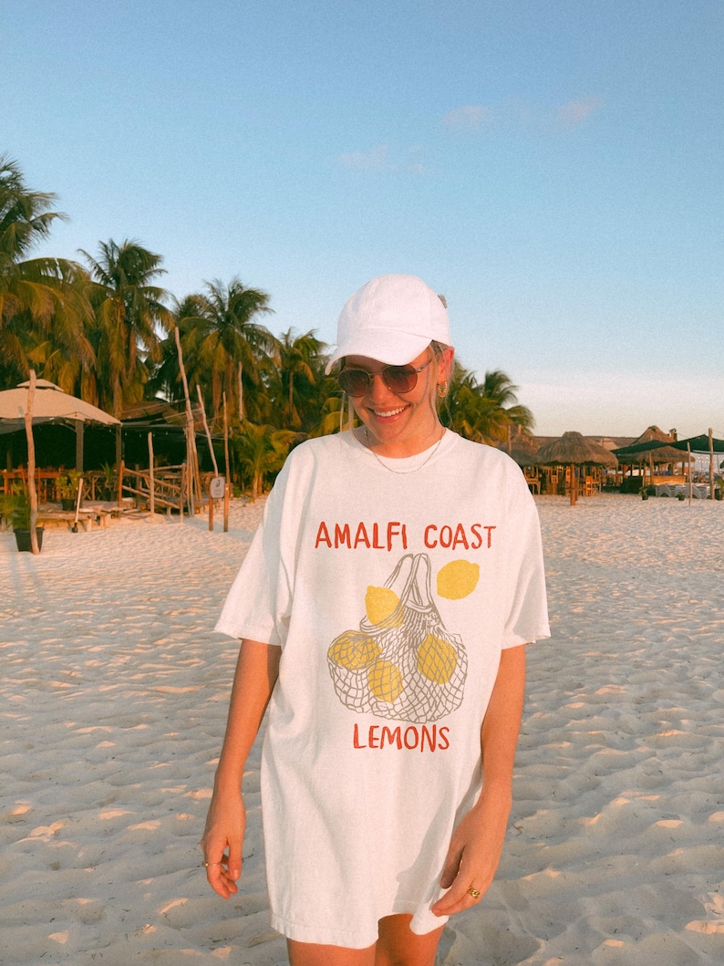 May include: White oversized t-shirt with a graphic of lemons in a mesh bag and the text "Amalfi Coast Lemons".