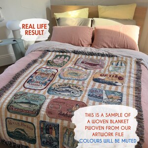 May include: Woven blanket with a sardine can design in various colors, displayed on a bed with pink pillows and a light-colored headboard. The blanket features a striped background and the text "THIS IS A SAMPLE OF A WOVEN BLANKET PWOVEN FROM OUR ARTWORK FILE COLOURS WILL BE MUTED."