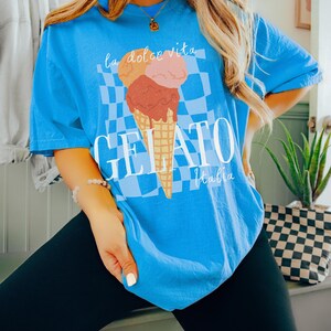 K&ouml;nnte beinhalten: Ein blaues T-Shirt mit einem Aufdruck eines dreist&ouml;ckigen Eisbechers mit dem Text "la dolce vita" dar&uuml;ber und "GELATO Italia" darunter.