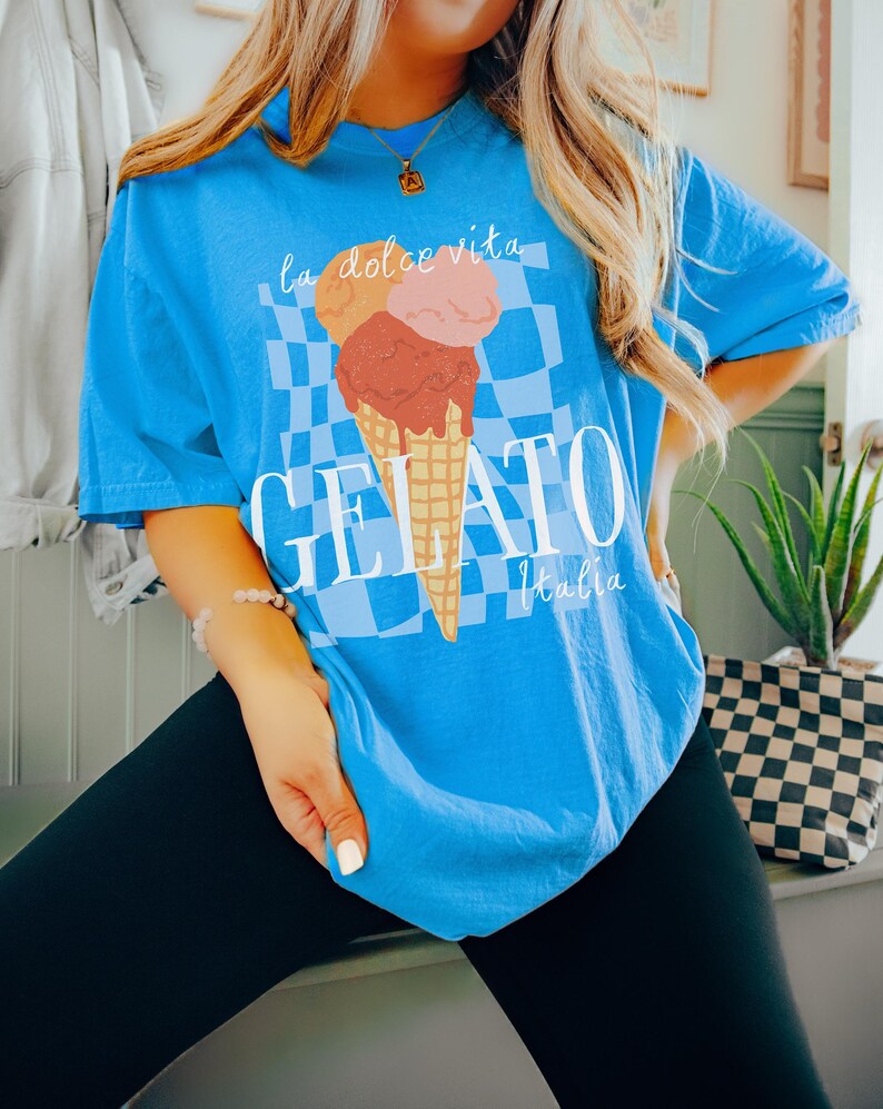 K&ouml;nnte beinhalten: Ein blaues T-Shirt mit einem Aufdruck eines dreist&ouml;ckigen Eisbechers mit dem Text "la dolce vita" dar&uuml;ber und "GELATO Italia" darunter.