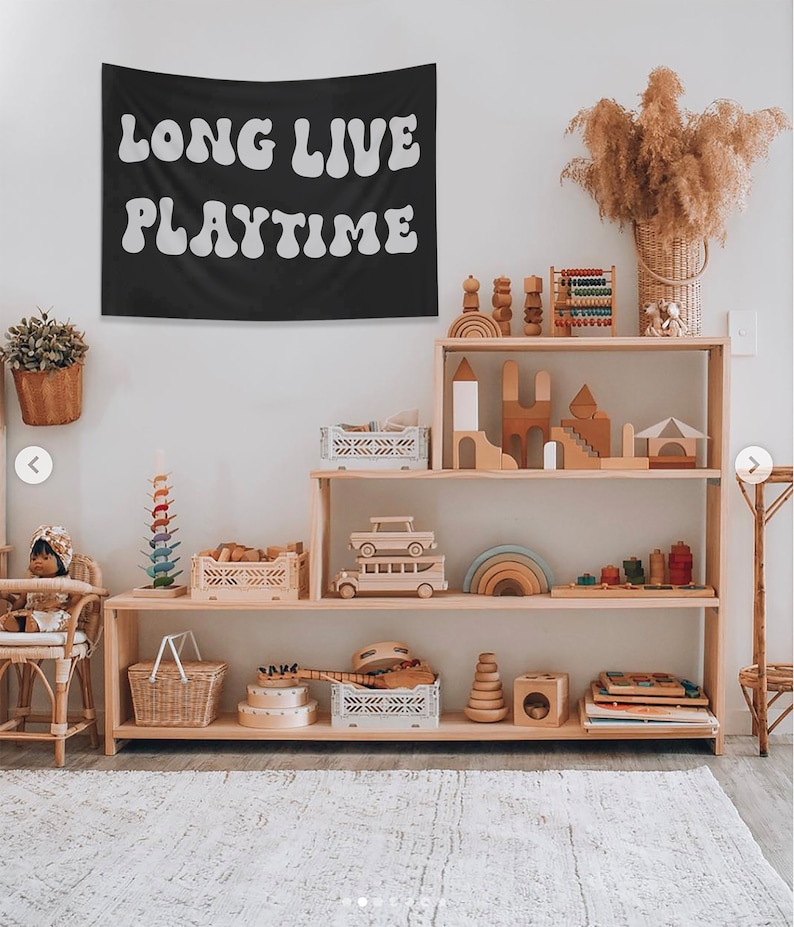 Puede incluir: Una estanter&iacute;a de madera con un tapiz negro colgado encima. El tapiz tiene las palabras "Long Live Playtime" en letras blancas y redondas. La estanter&iacute;a est&aacute; llena de juguetes de madera, incluyendo un &aacute;baco de madera, un castillo de madera y un coche de madera. Tambi&eacute;n hay cestas y cajas en las estanter&iacute;as.