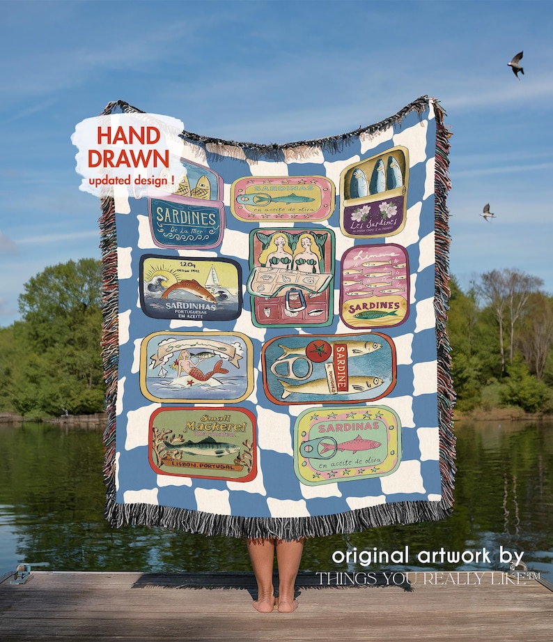 May include: A blue and white checkered throw blanket featuring colorful sardine tin illustrations. The blanket has a fringed edge and text that reads "HAND DRAWN updated design!" and "original artwork by THINGS YOU REALLY LIKE!"