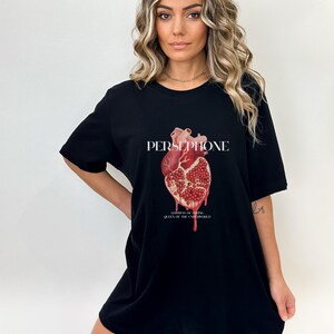 May include: Black t-shirt with a graphic of a red heart made of a pomegranate. The text "PERSEPHONE, GODDESS OF SPRING, QUEEN OF THE UNDERWORLD" is printed below the graphic.