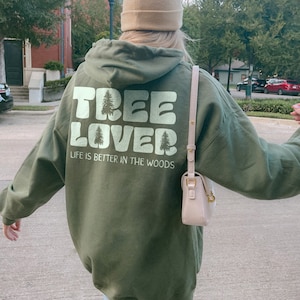 May include: A green hooded sweatshirt with the text "TREE LOVER" and "LIFE IS BETTER IN THE WOODS" printed on the back. The sweatshirt has a large hood and a relaxed fit.