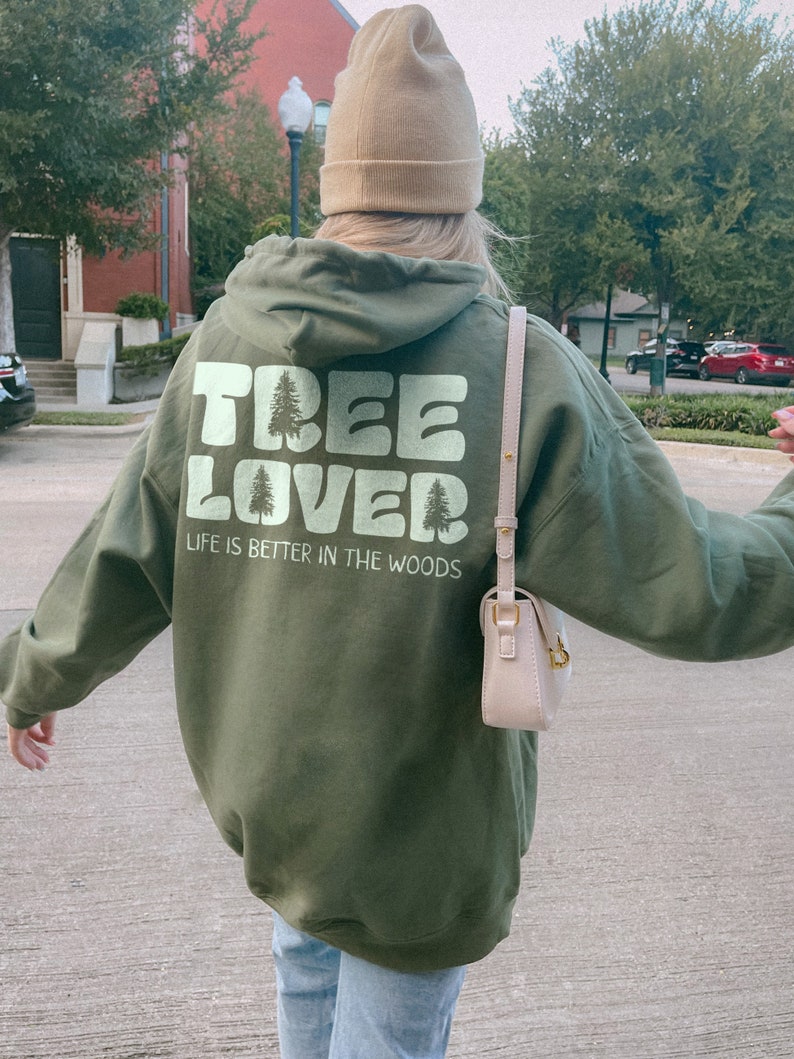 May include: A green hooded sweatshirt with the text "TREE LOVER" and "LIFE IS BETTER IN THE WOODS" printed on the back. The sweatshirt has a large hood and a relaxed fit.