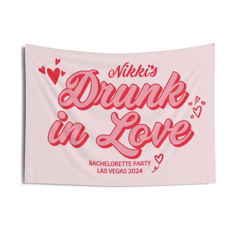 May include: Pink bachelorette party banner with the text "Nikki's Drunk in Love" in red and white lettering. The banner also includes the text "Bachelorette Party Las Vegas 2024" and several small red hearts.