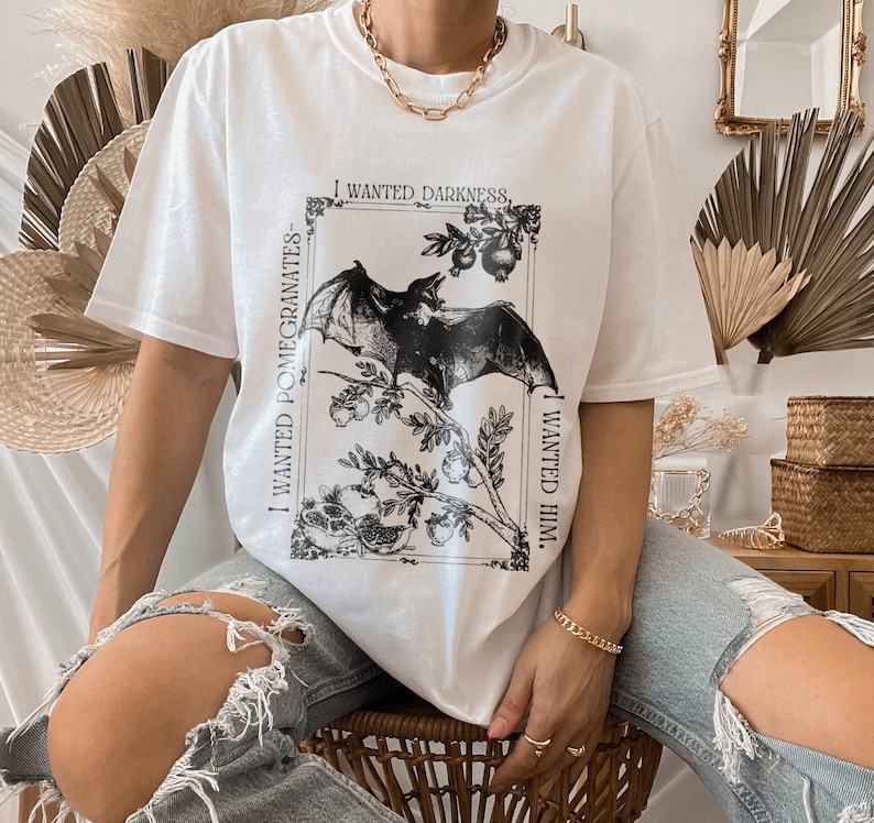 May include: White t-shirt with a black and white graphic print of a bat and pomegranates. The text on the shirt reads "I wanted darkness, I wanted pomegranates, I wanted him."