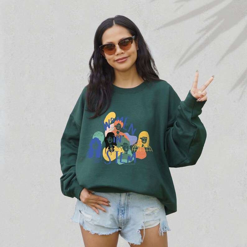 May include: A dark green sweatshirt with a graphic print of women in STEM. The graphic features colorful illustrations of women's faces and the text "Women in STEM".
