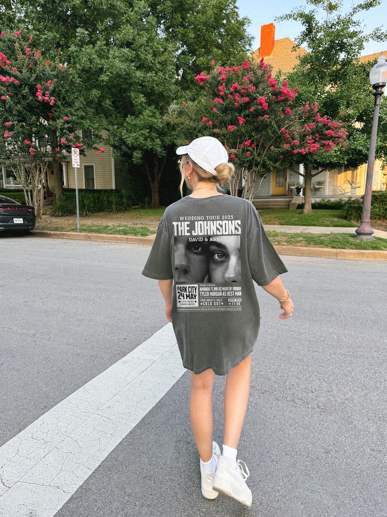 May include: A gray oversized t-shirt with a black and white graphic print of a wedding announcement for "The Johnsons" with the text "Wedding Tour 2025" and "David & Anha". The graphic also includes a black and white photo of a couple and the text "Park City 24 May".