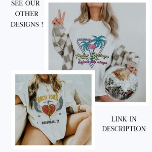 May include: Two white t-shirts with different graphic designs. The first shirt features a pink flamingo and palm trees with the text "California Palm Springs before the rings". The second shirt features a red heart with lightning bolt and wings with the text "Bach Tour 20 Nashville, TN 23".