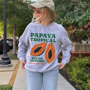 Puede incluir: Sudadera gris con un gr&aacute;fico de papaya y el texto "PAPAYA TROPICAL RIO DE JANEIRO Feira de Copacabana".
