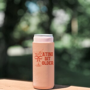 May include: A peach-colored can cooler with a martini glass graphic and the text "A TINI BIT OLDER" in red.