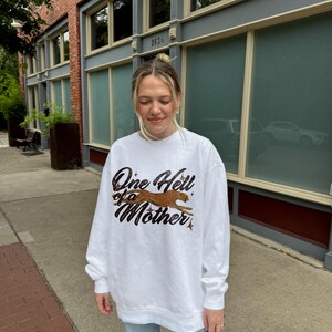 Peut inclure: Sweat-shirt blanc avec un imprim&eacute; graphique d'un gu&eacute;pard courant et le texte "One Hell of a Mother".